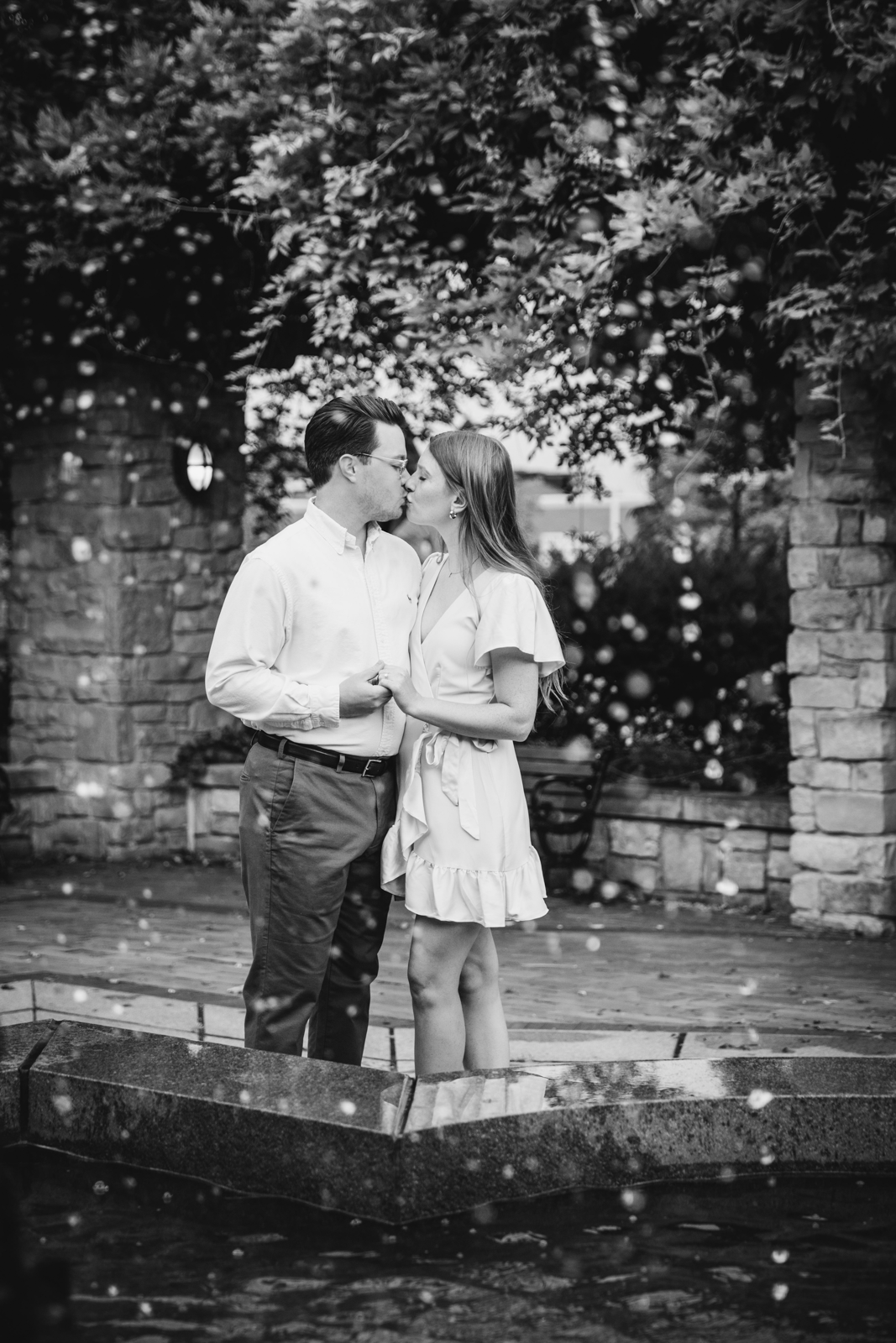  Engaged couple kisses on the other side of a fountain in downtown Syracuse NY 