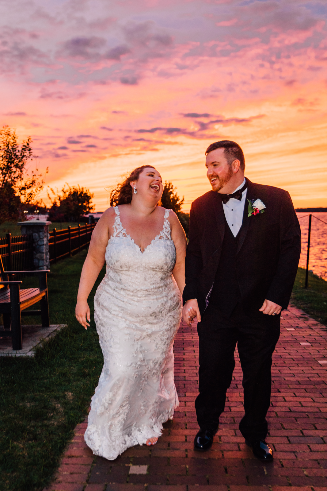  Bride and Groom laugh while walking hand-in-hand during sunset wedding photos in Clayton NY 