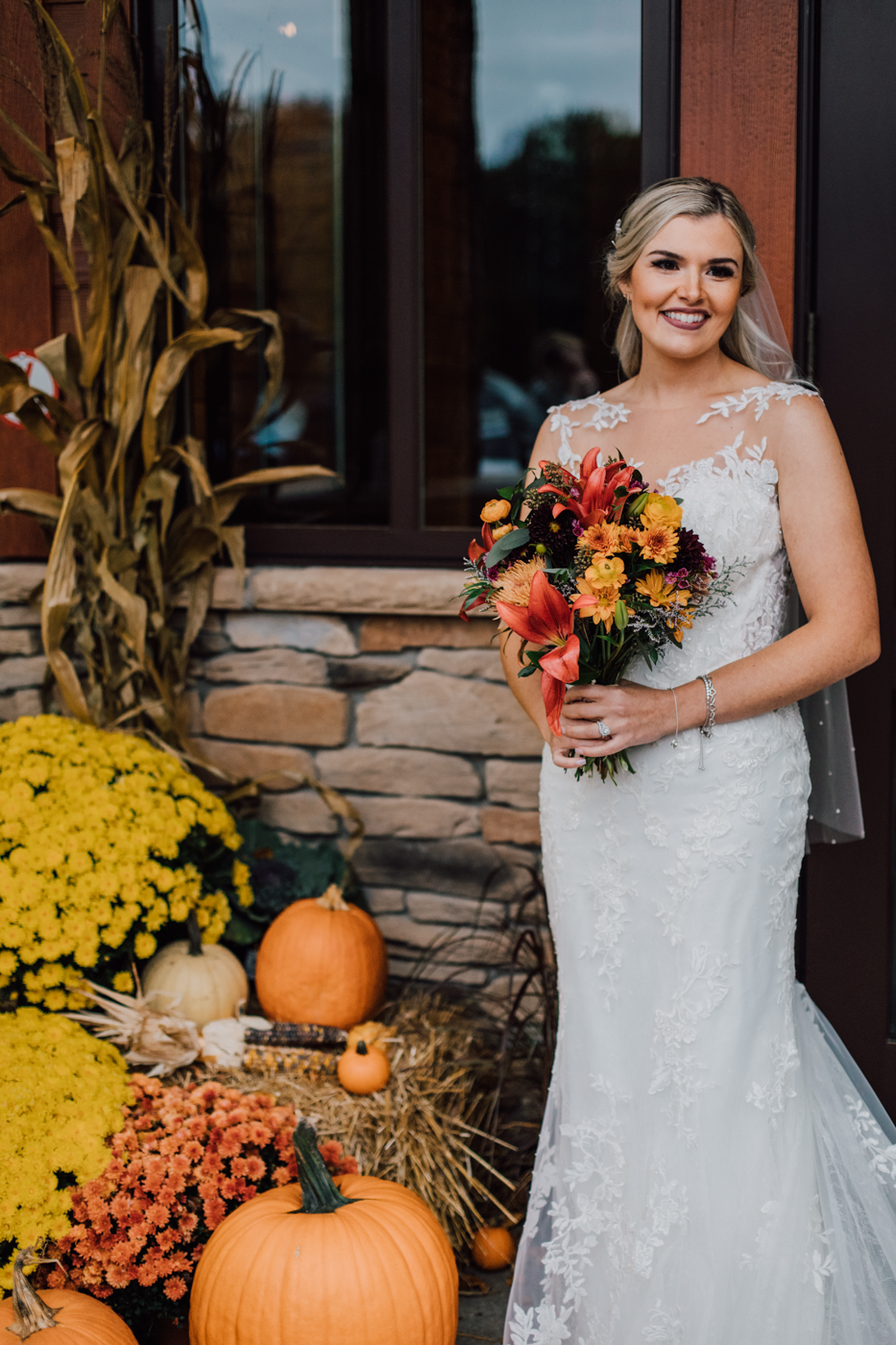  Bride poses for fall wedding photos near some mums and pumpkins outside Tailwater Lodge 