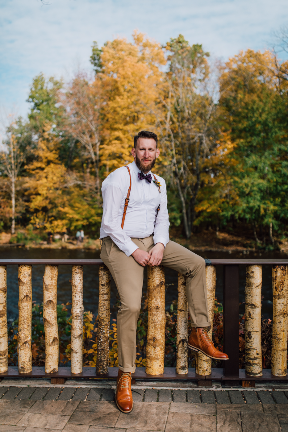  Groom sits on the edge of a bridge during fall wedding photos at Tailwater Lodge 