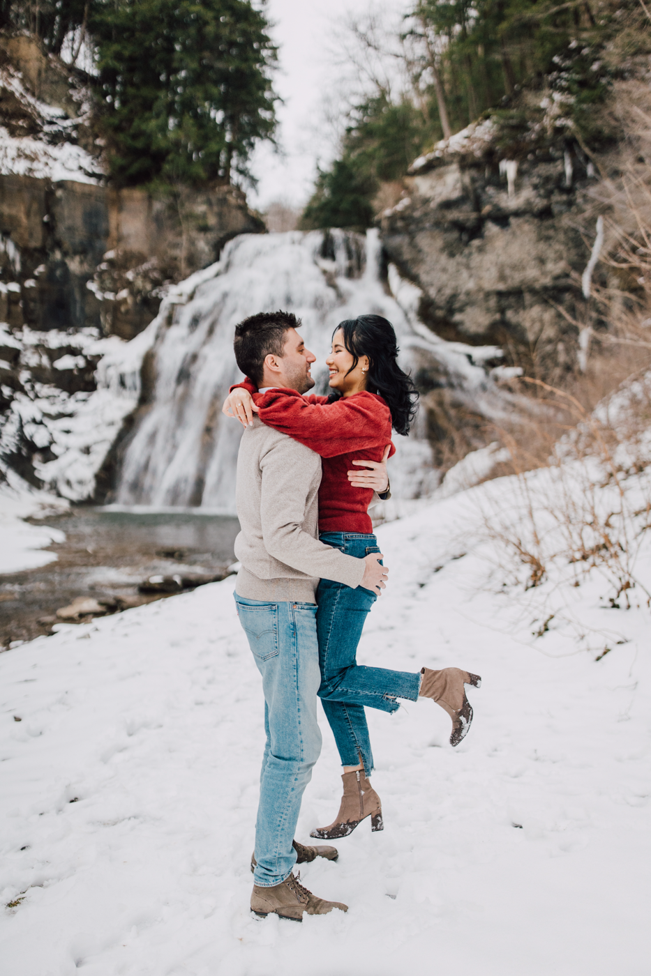  Man lifts up his fiance during their snowy engagement photos at a waterfall in central NY 