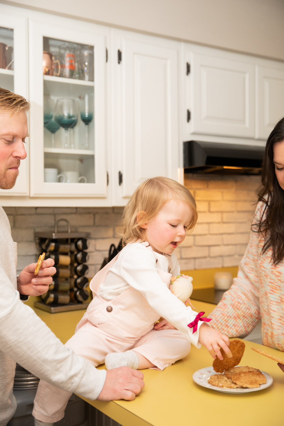  Toddler reaches for a cookie while sitting on the kitchen counter during a family photoshoot at home in Central NY 