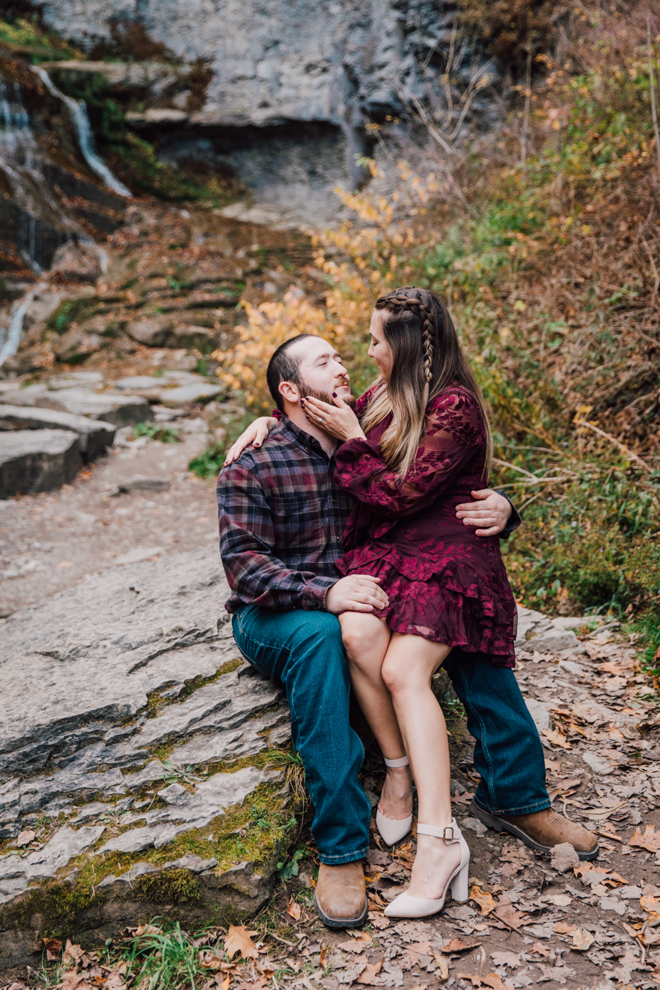  Woman sits on her fiance’s lap during their fall engagement photos at Delphi Falls County Park 