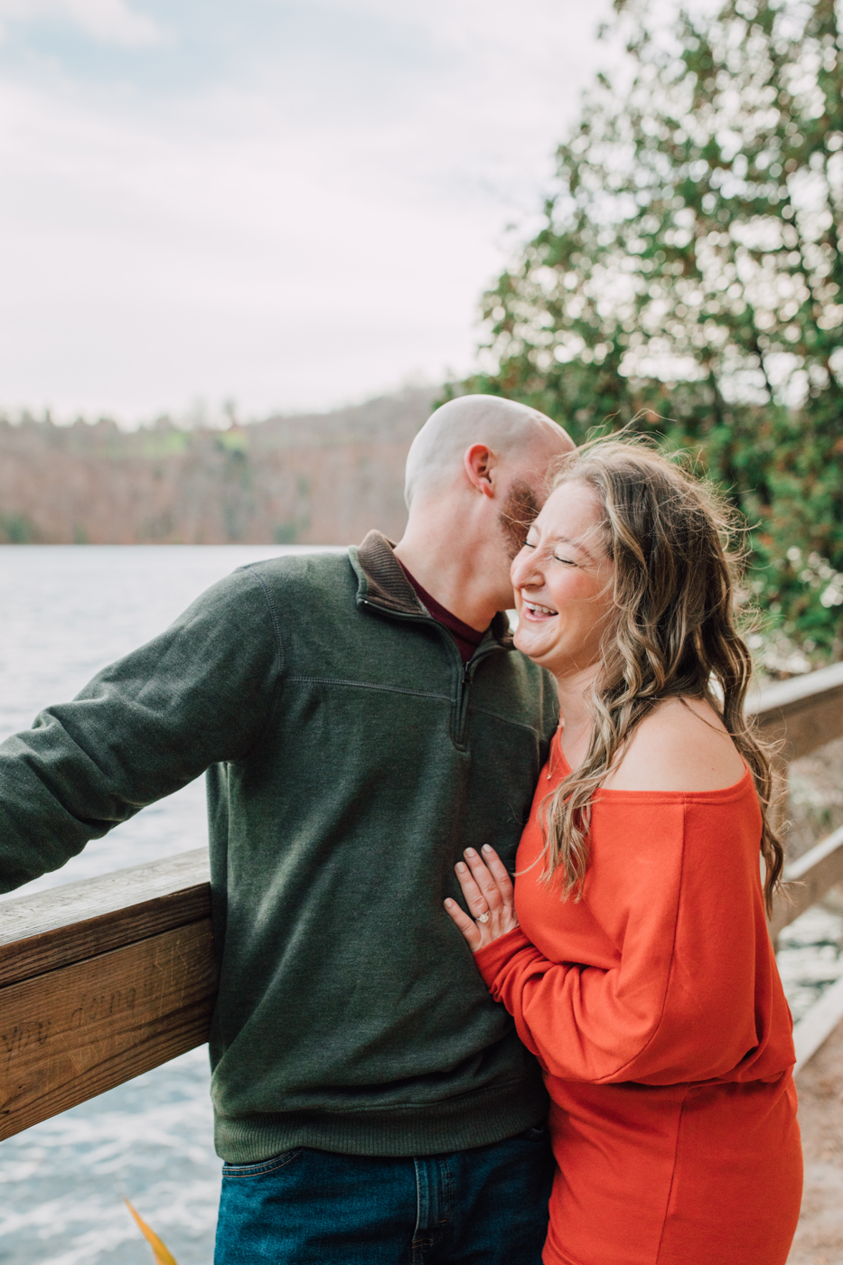  Engaged couple laughs while standing on a bridge together for their cozy fall pictures 