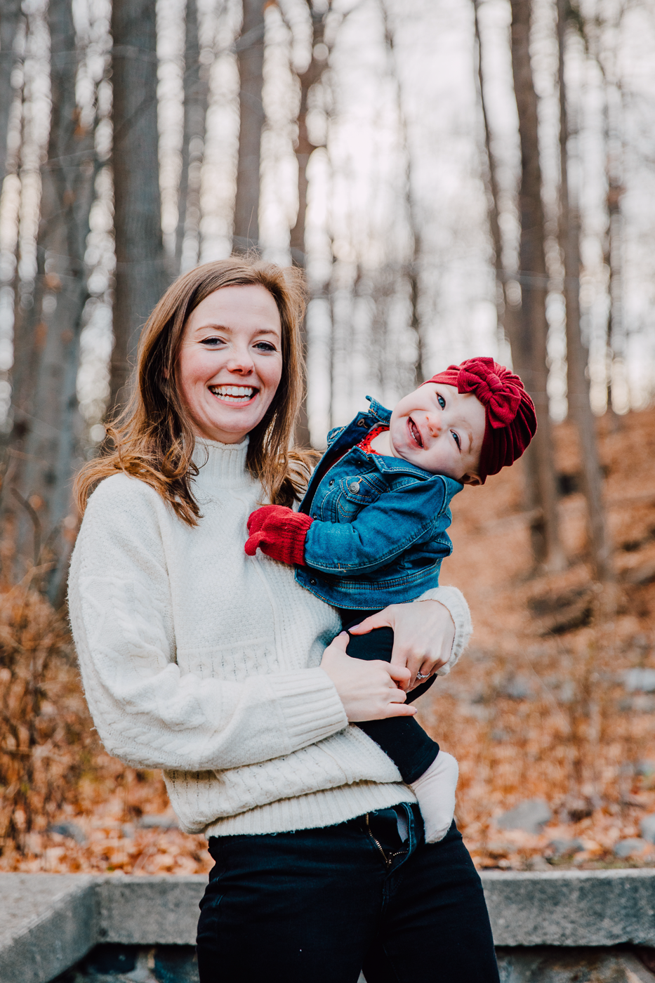  Young mom holds her infant daughter while taking family photos in the woods in winter 