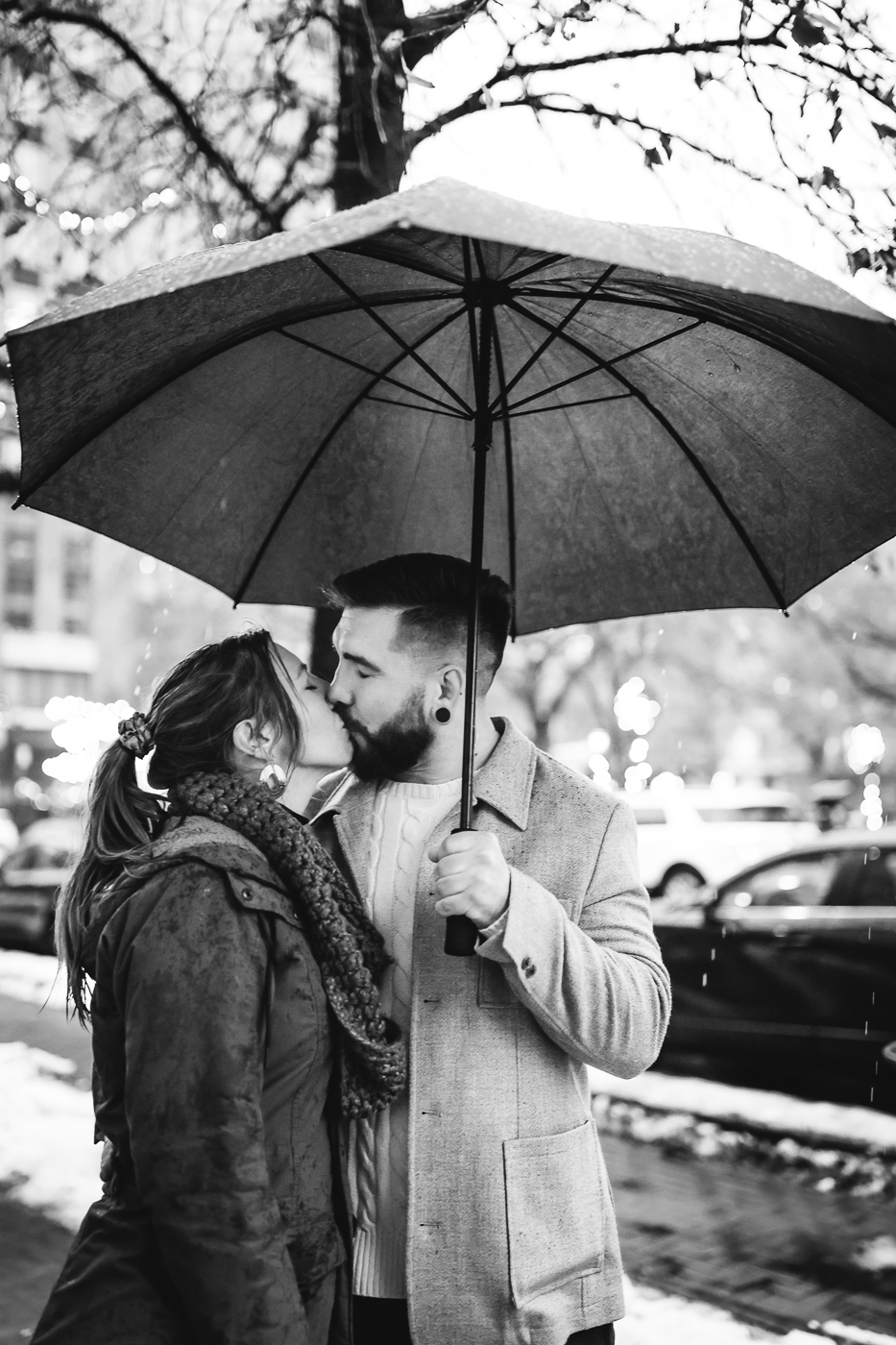  Engaged couple kisses underneath an umbrella during their rainy proposal in downtown Syracuse 