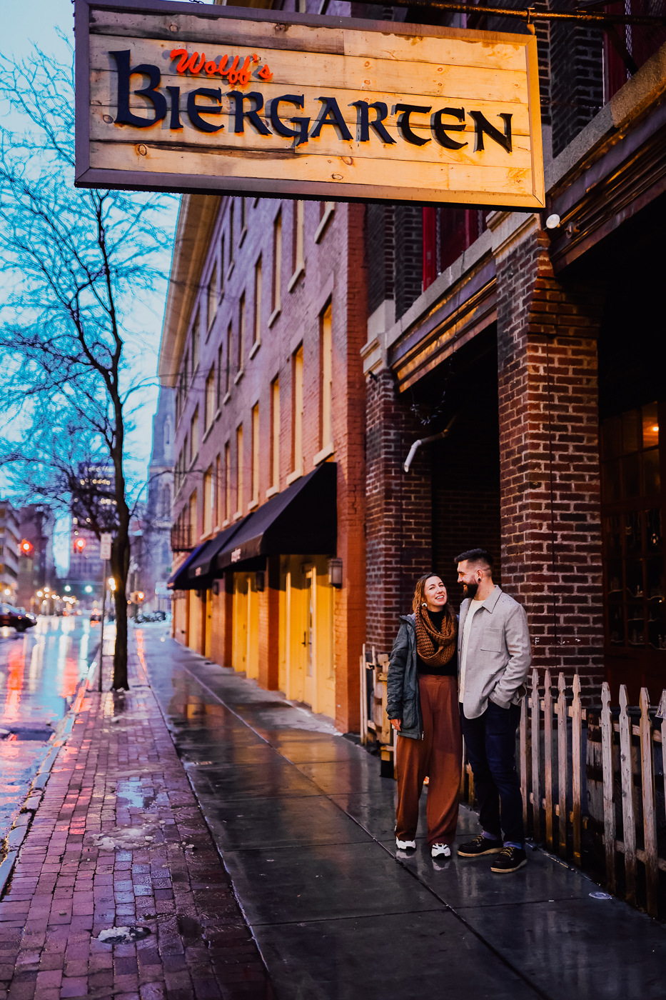  Engaged couple stands in front of Wolff’s Biergarten in downtown Syracuse  