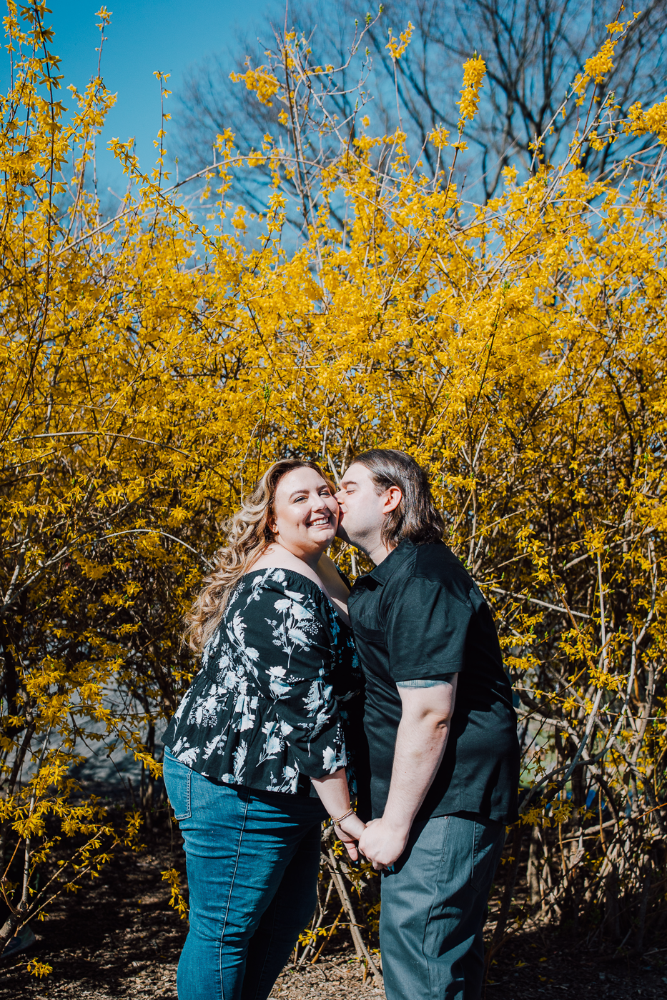  man kisses his fiance on the cheek surrounded by forsythia in Central Park in spring 