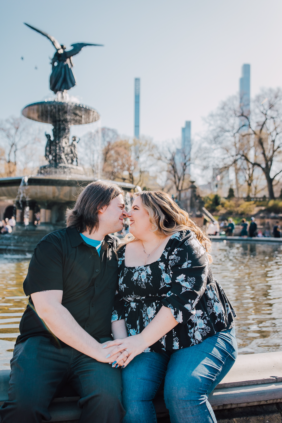  Engaged couple sit face-to-face in front of the Bethesda Fountain in Central Park during their spring engagement photos 
