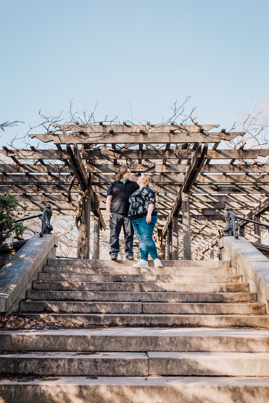  engaged couple stands at the top of a set of stairs while taking Central Park engagement photos   