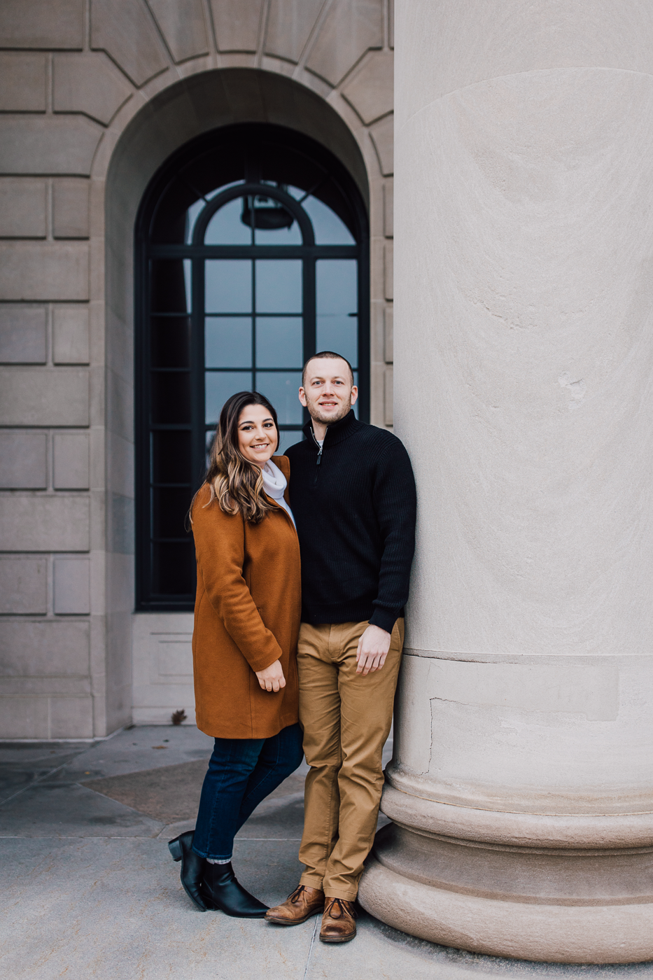  Engaged couple stands together in front of a stone building in downtown Syracuse during their winter engagement photos 