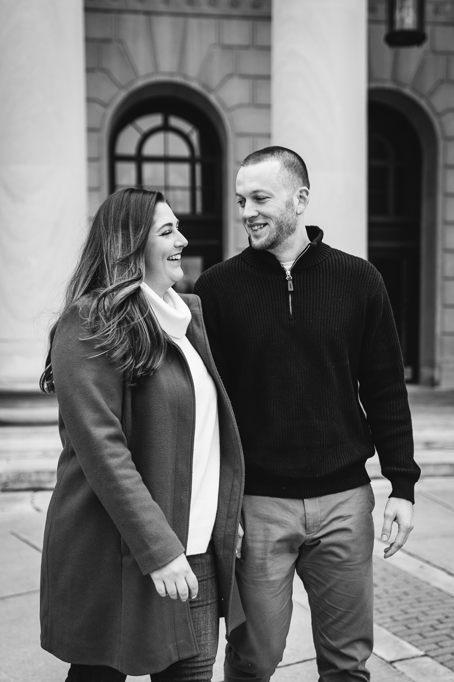  Engaged couple laugh as they walk together near Clinton Square in downtown Syracuse during their winter engagement photos 