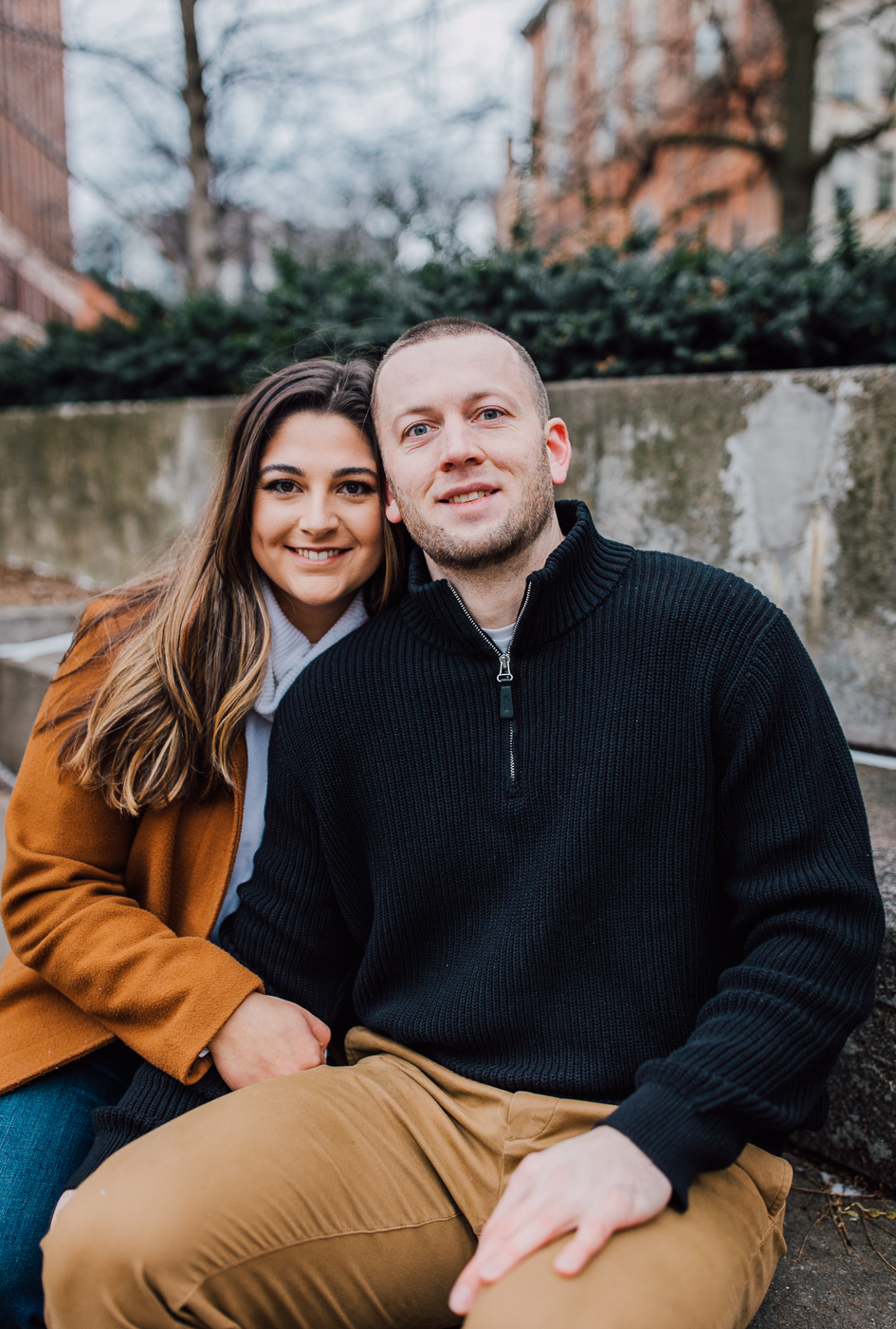  Engaged couple cuddles up in Hanover Square in downtown Syracuse while taking winter engagement photos 