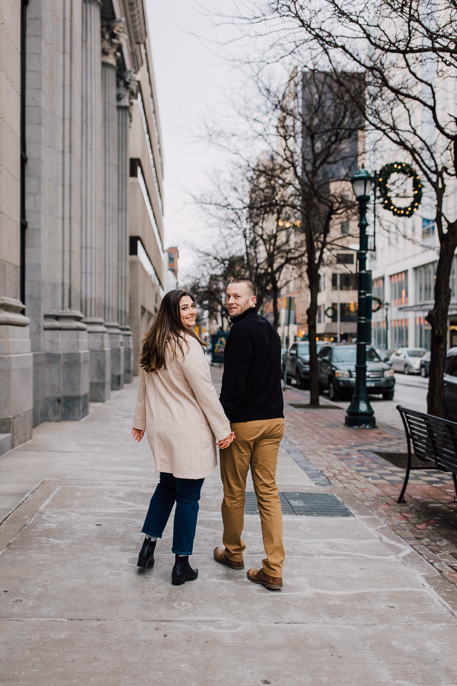  Engaged couple holds hands while walking through downtown Syracuse during their winter photo shoot 
