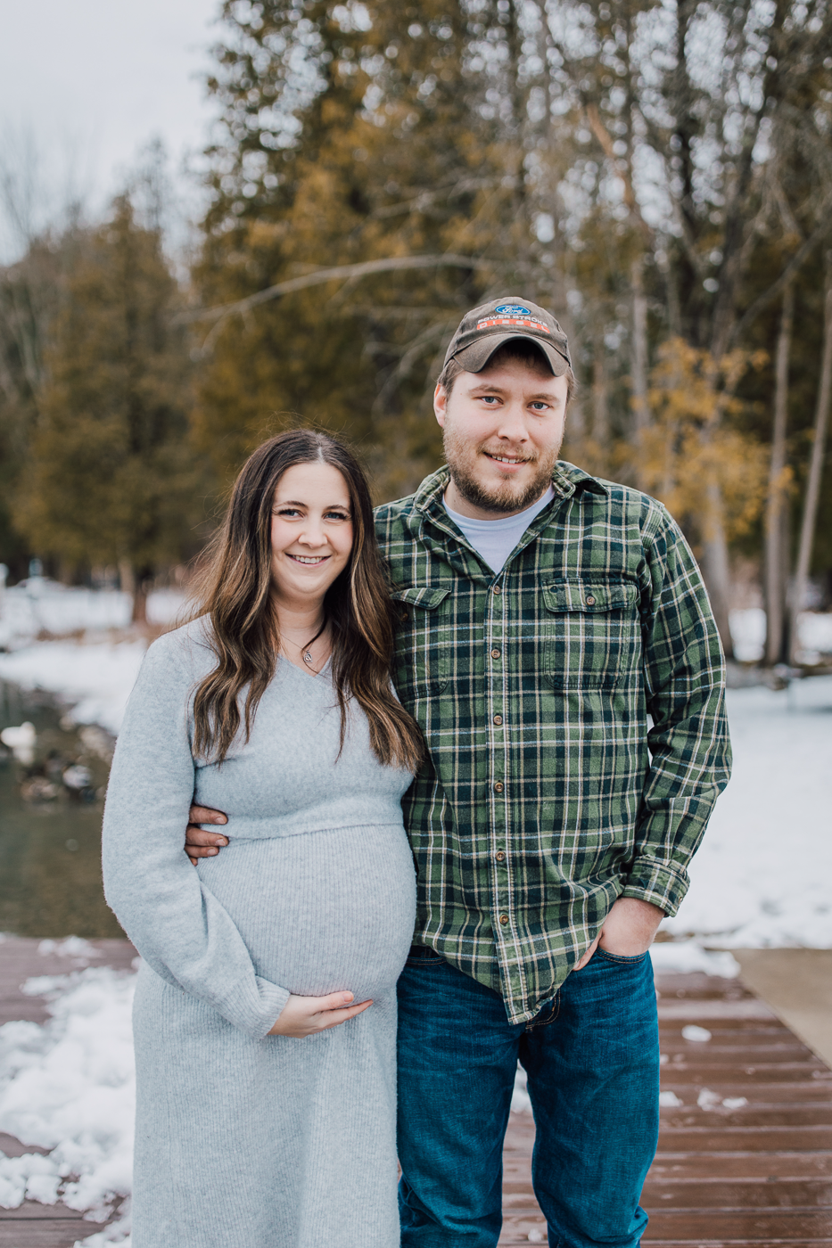  Pregnant woman and her husband stand by the lake during their twins pregnant announcement at Green Lakes State Park in winter 