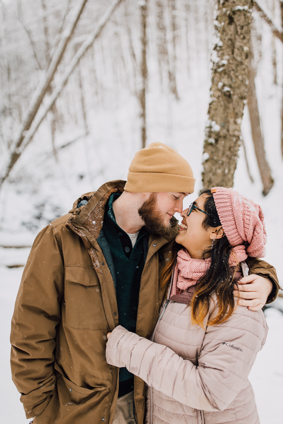  Engaged couple stand nose-to-nose at Tinker Falls while taking winter wonderland photos with Brittany Juravich 