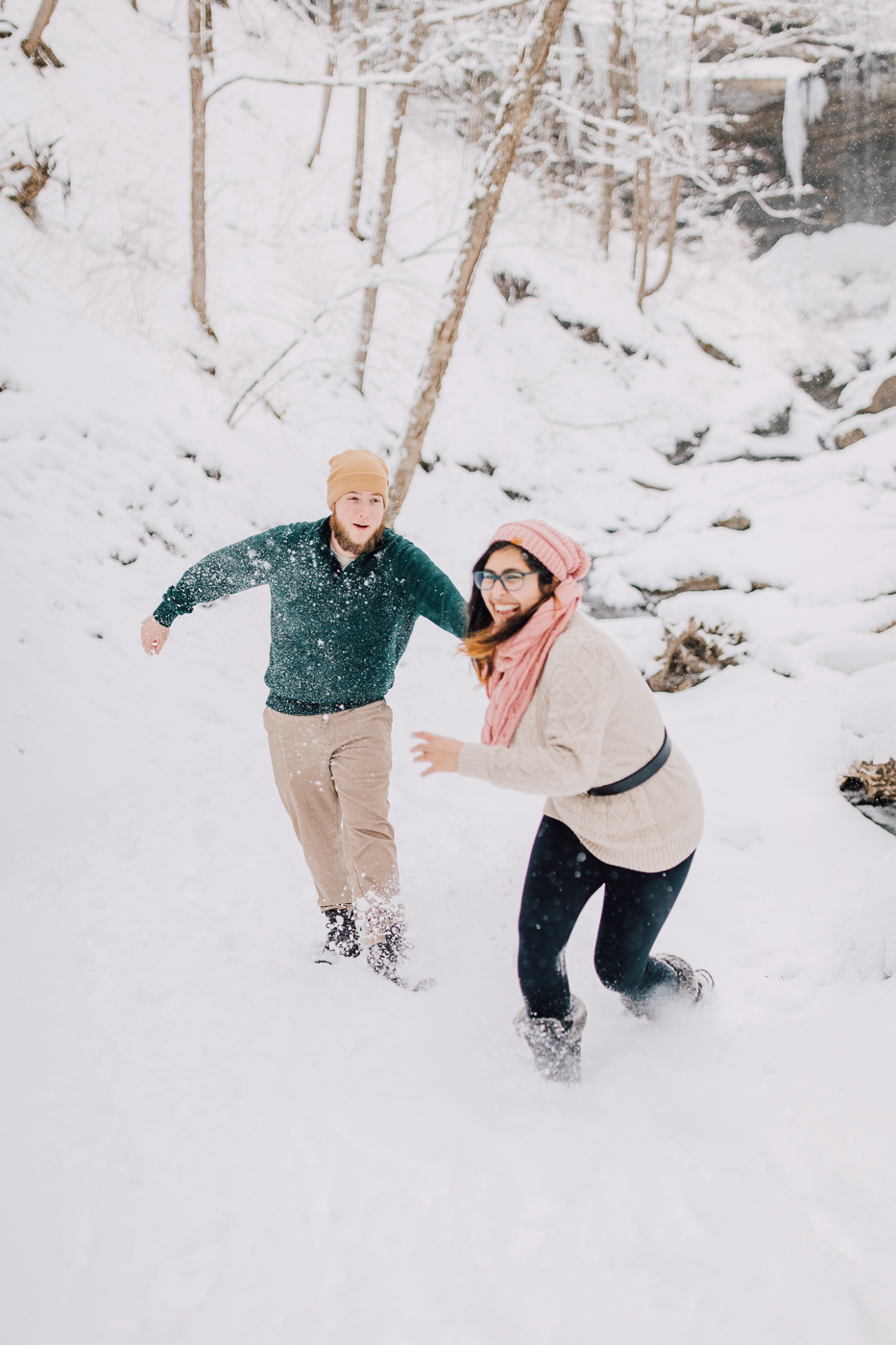  Engaged couple has a snowball fight during their adventure photoshoot at Tinker Falls in winter 