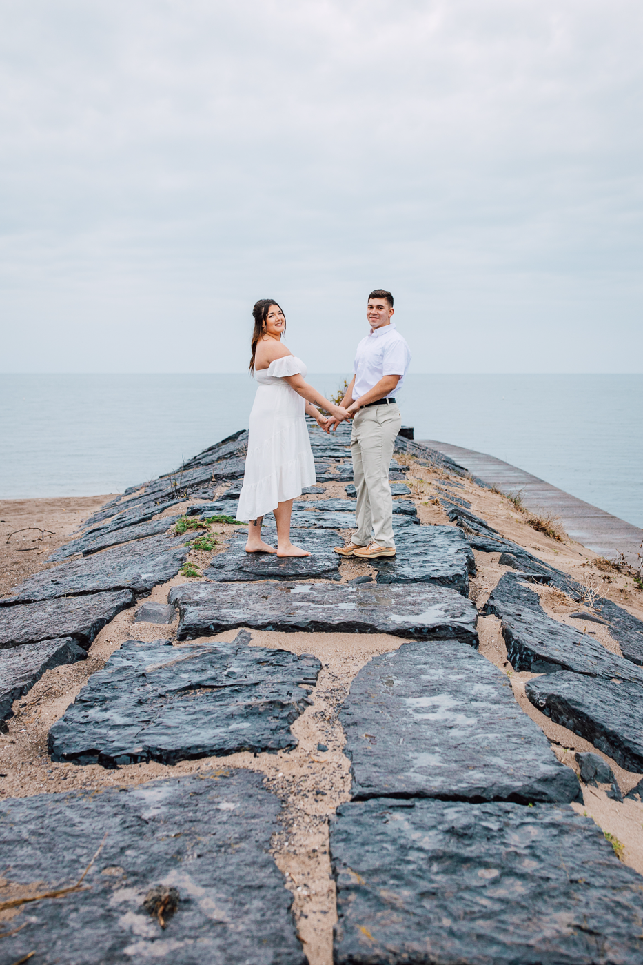  Engaged couple stands on a breakwall during their beach engagement photos at Fair Haven State Park in Central NY 