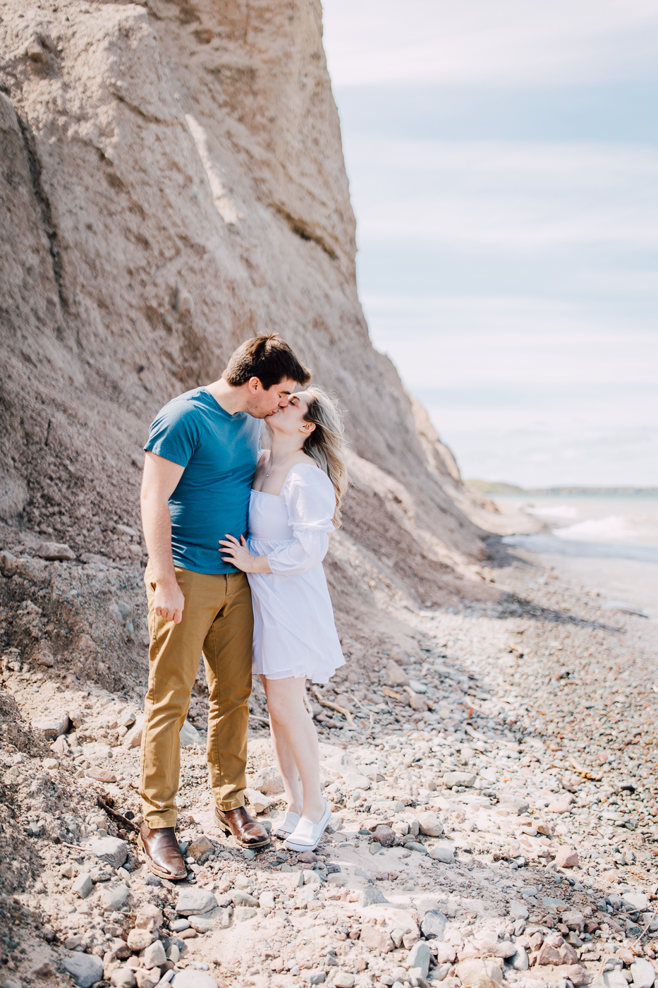  Engaged couple kisses on the beach below Sterling Bluffs along the shores of Lake Ontario during their spring engagement photos 