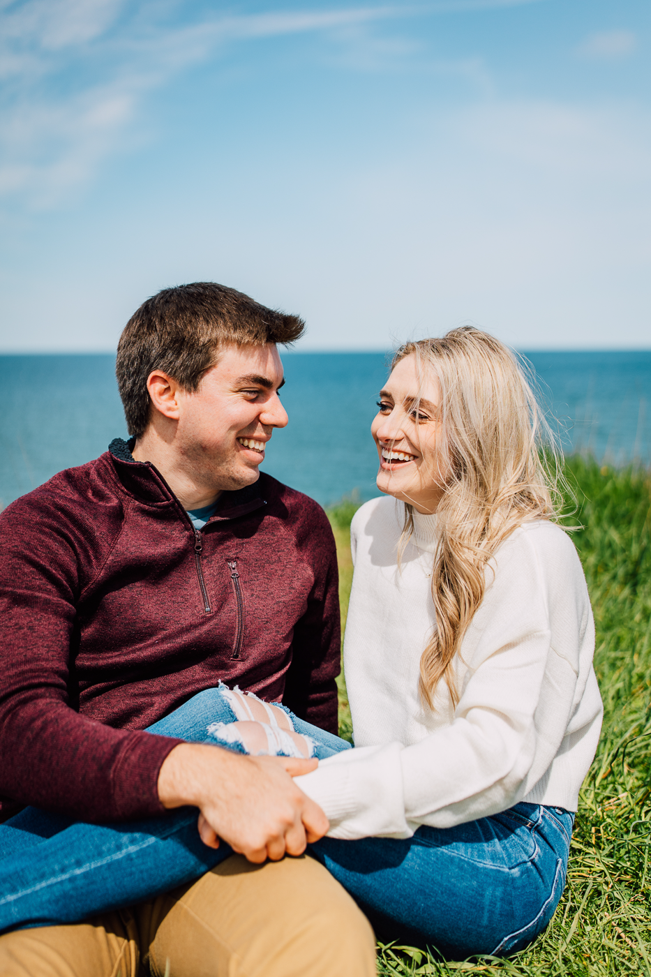  Engaged couple laugh together while sitting on Sterling Bluffs in Central NY during their spring engagement photos 