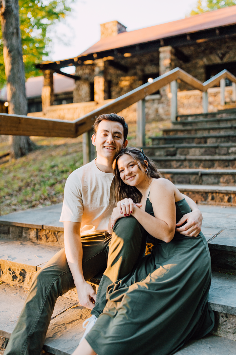  Engaged couple sits together on a set of stairs at Green Lakes State Park as the sun sets during their summer engagement photos 