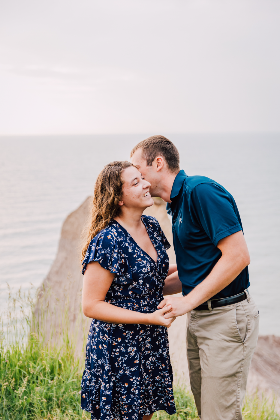  Man kisses his fiance on the cheek overlooking Lake Ontario during their summer engagement photos 