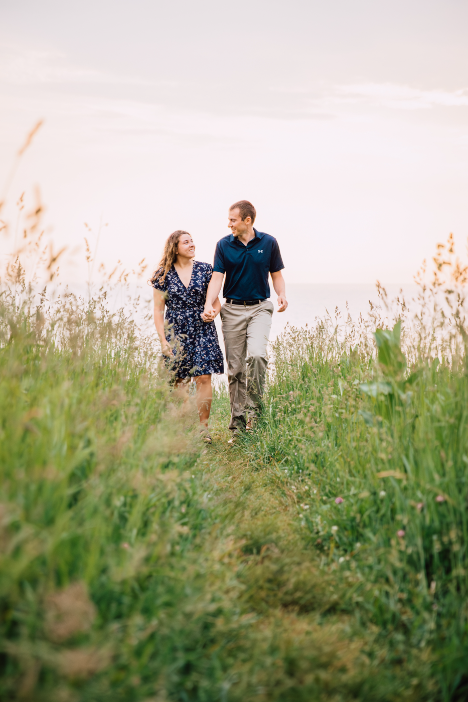  Engaged couple walks along the Oswego Bluffs with Lake Ontario in the background during their lake engagement photos 