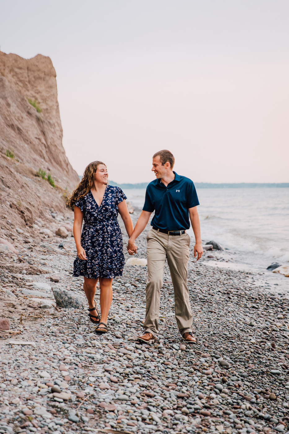  Engaged couple walks along the rocky shore of Lake Ontario during their engagement session with Brittany Juravich 