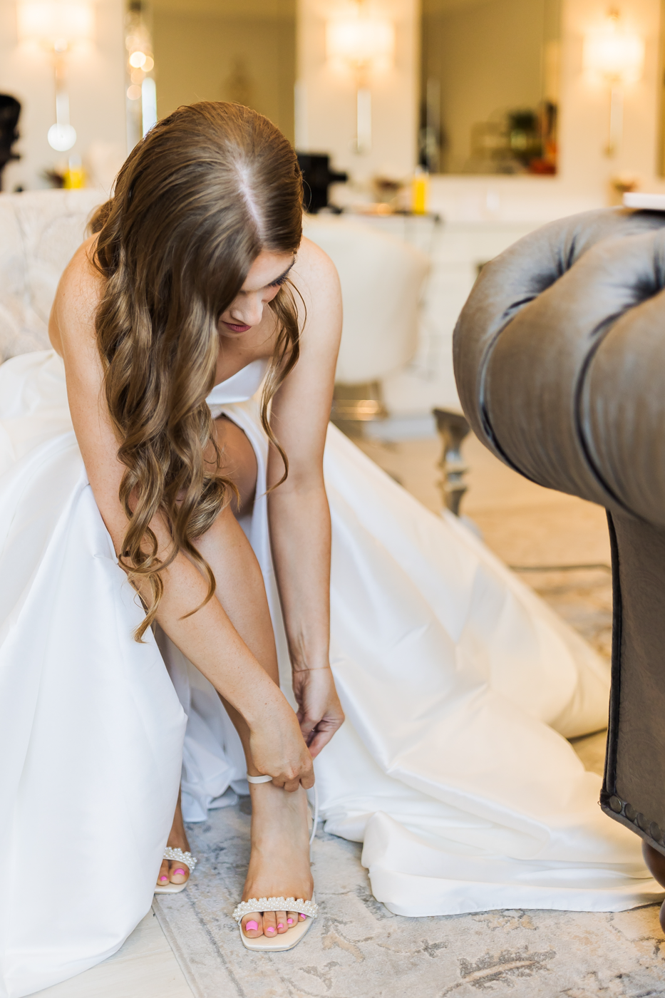 Bride bends down to fasten her shoe while getting ready for her ballroom wedding in Baldwinsville NY 