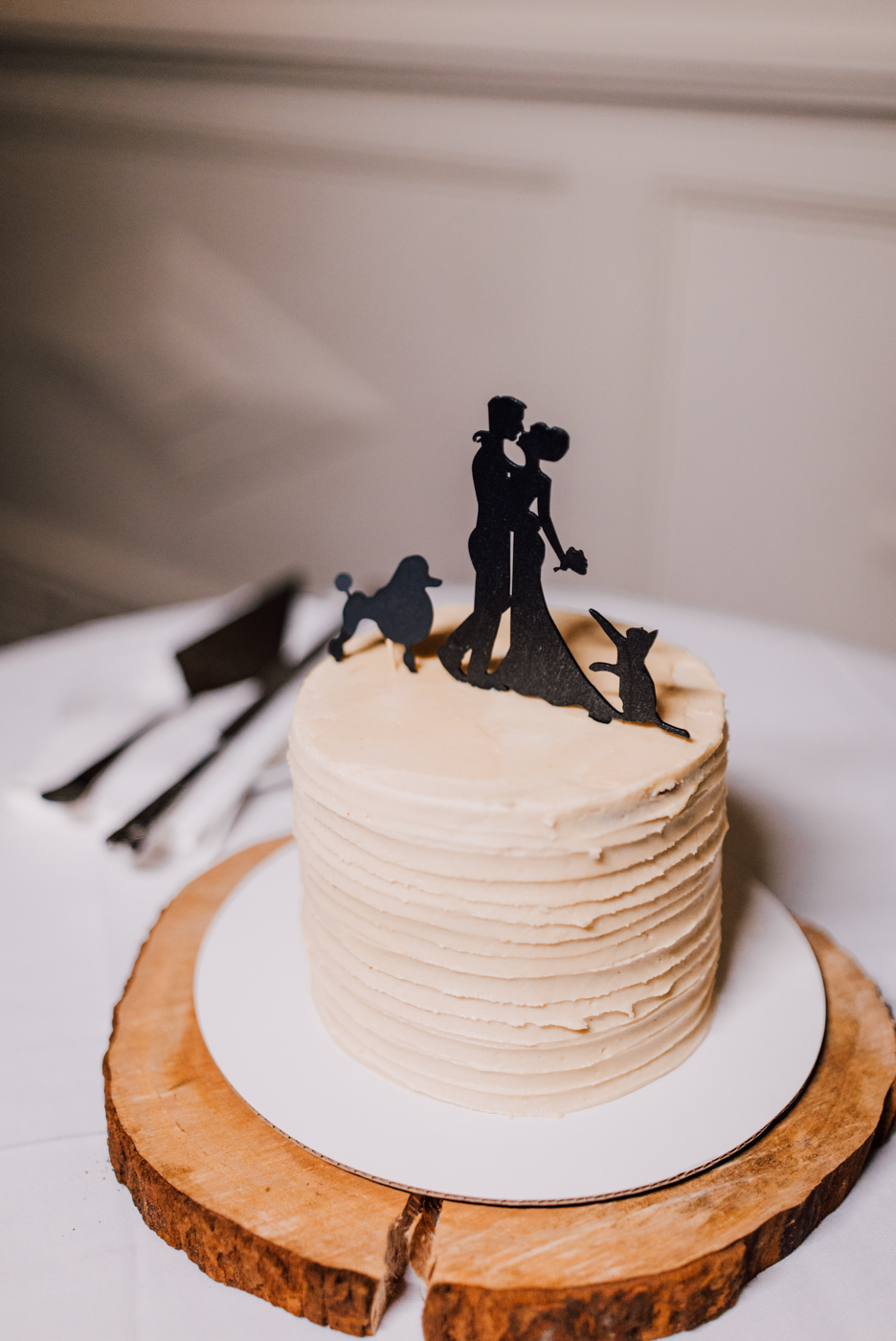  Small 1-tier wedding cake with silhouette cake topper, sitting atop a slice of wood 