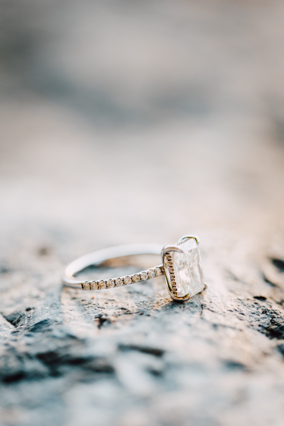  Close-up of a diamond solitaire radiant-cut engagement ring sitting on a rock 