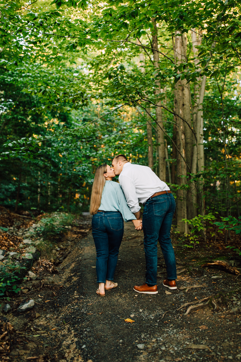  Engaged couple kiss as they walk hand-in-hand through the forest at Green Lakes State Park 