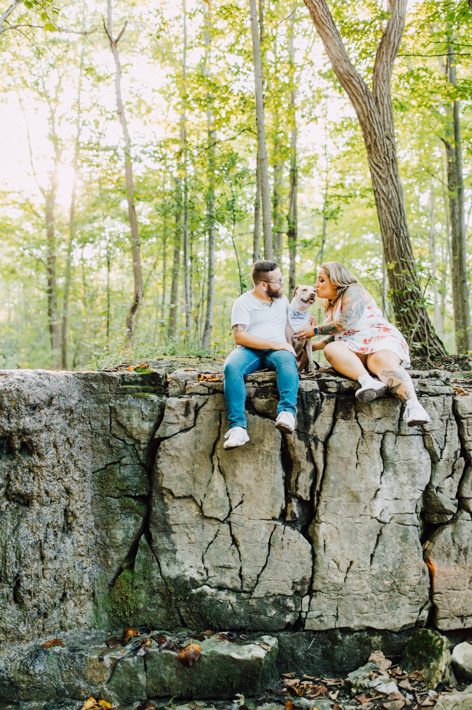  Engaged couple sits atop a small cliff with their dog at Three Falls Woods for an adventure photoshoot with Brittany Juravich 
