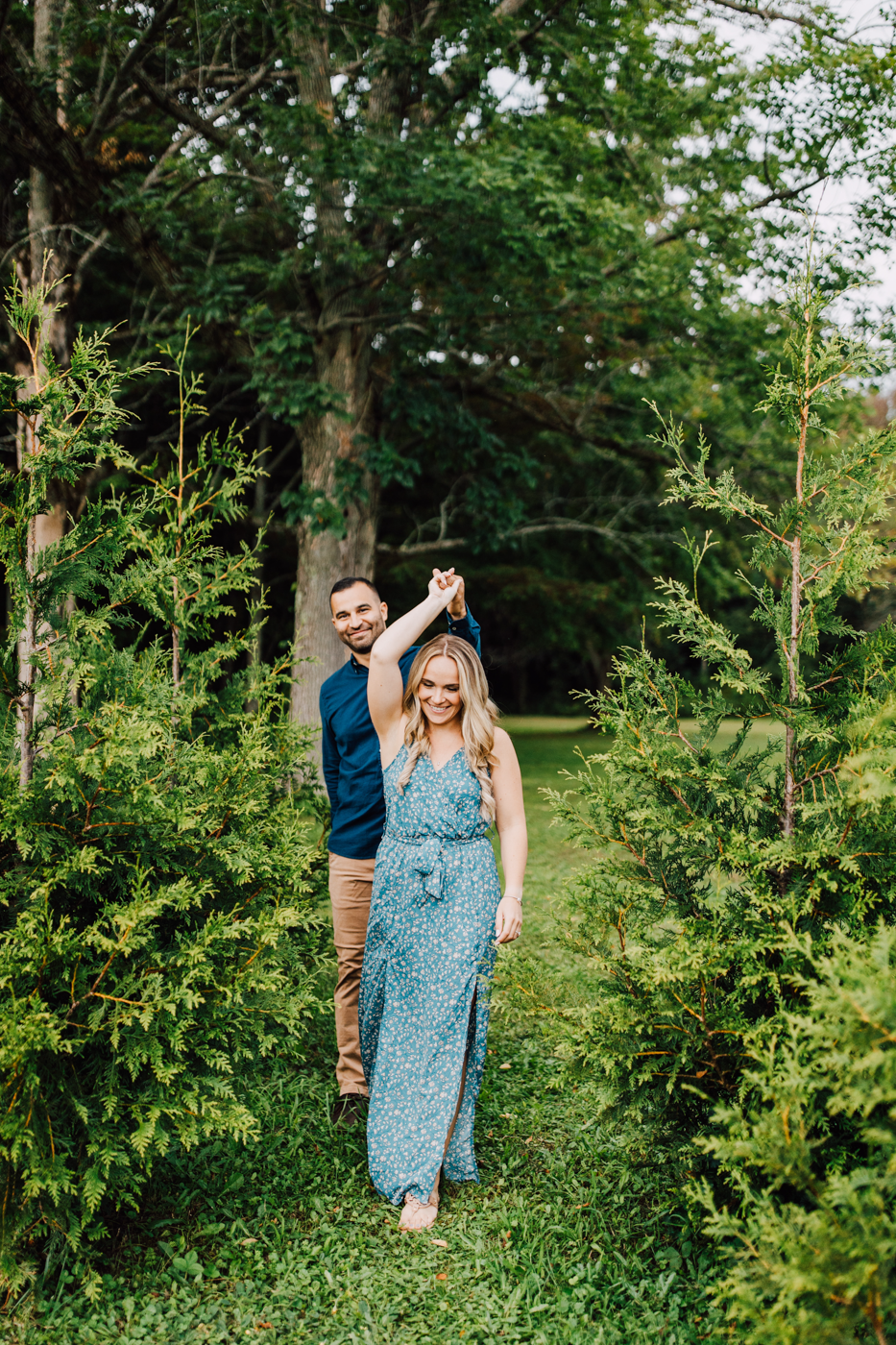  Woman leads her fiance through a grove of pine trees during their timeless engagement photos in Oswego NY 