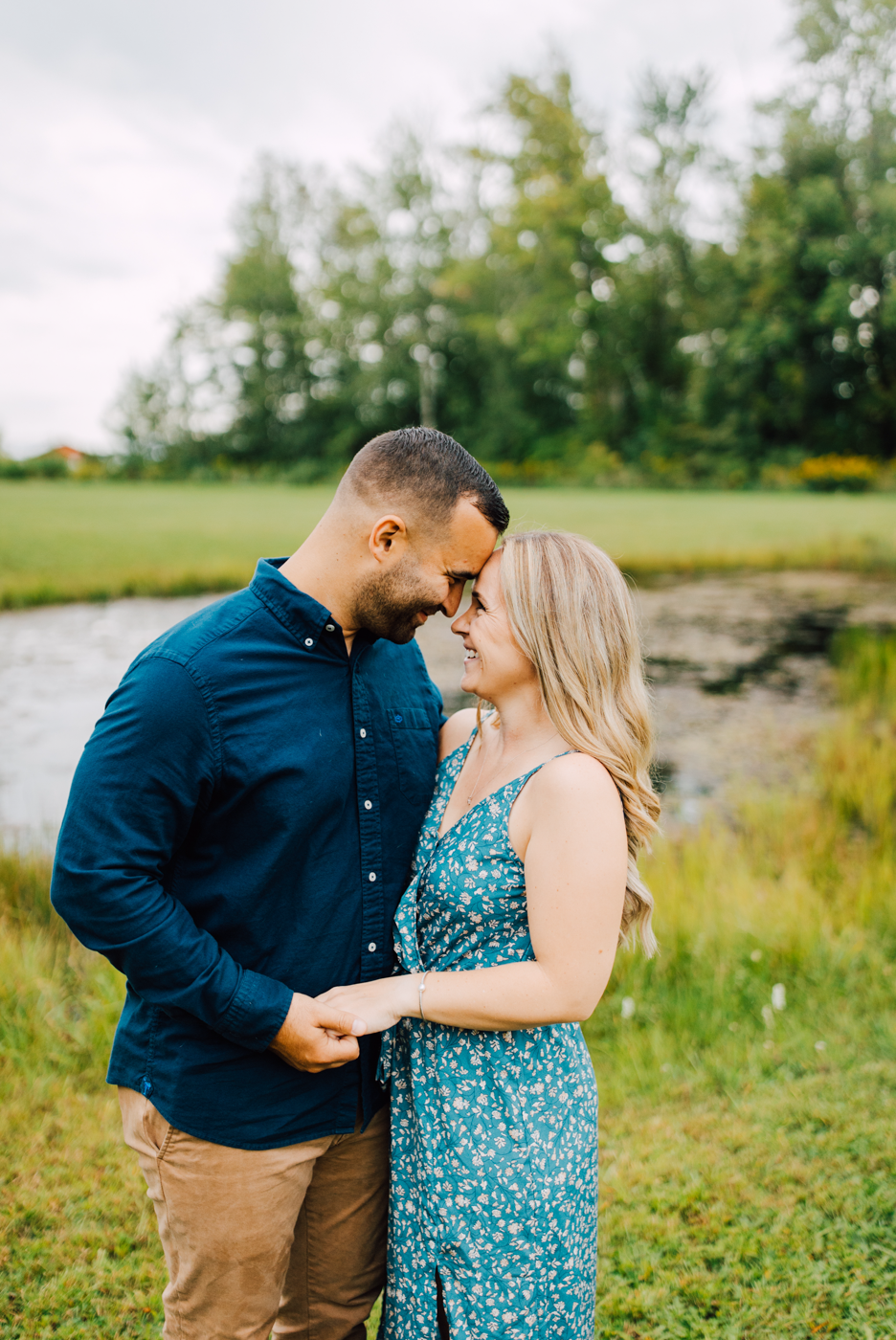 Engaged couple stands forehead-to-forehead during their field engagement photos on their property in Oswego NY 