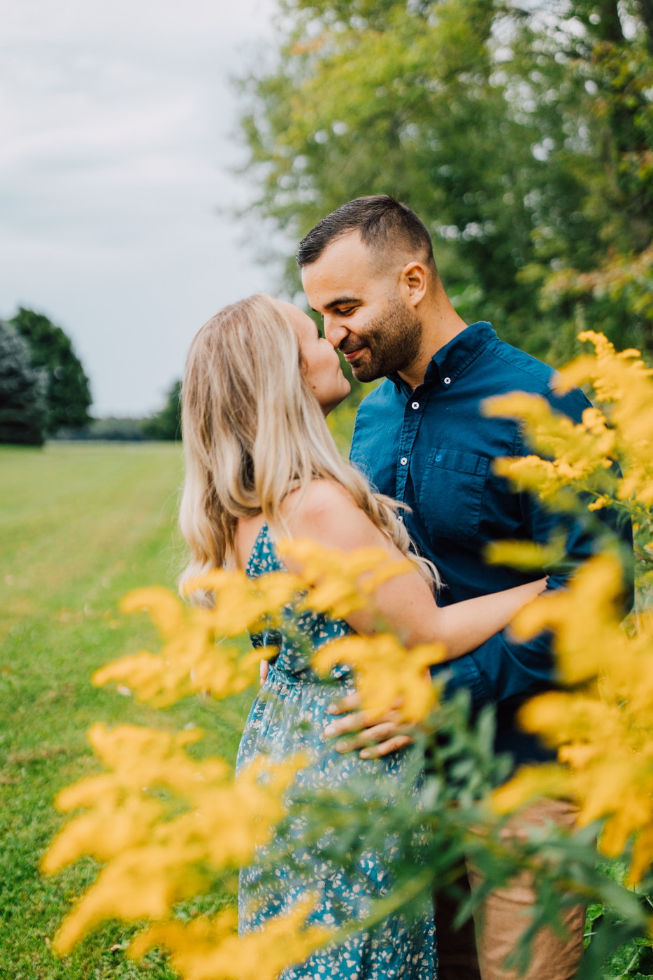  Engaged couple embrace face-to-face near some wildflowers during their field engagement photos in central nY 