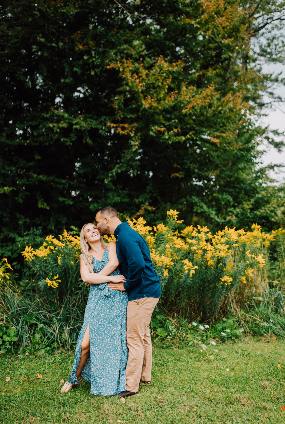  Man kisses his fiance on the cheek in front of a patch of wildflowers on their property in Central NY 