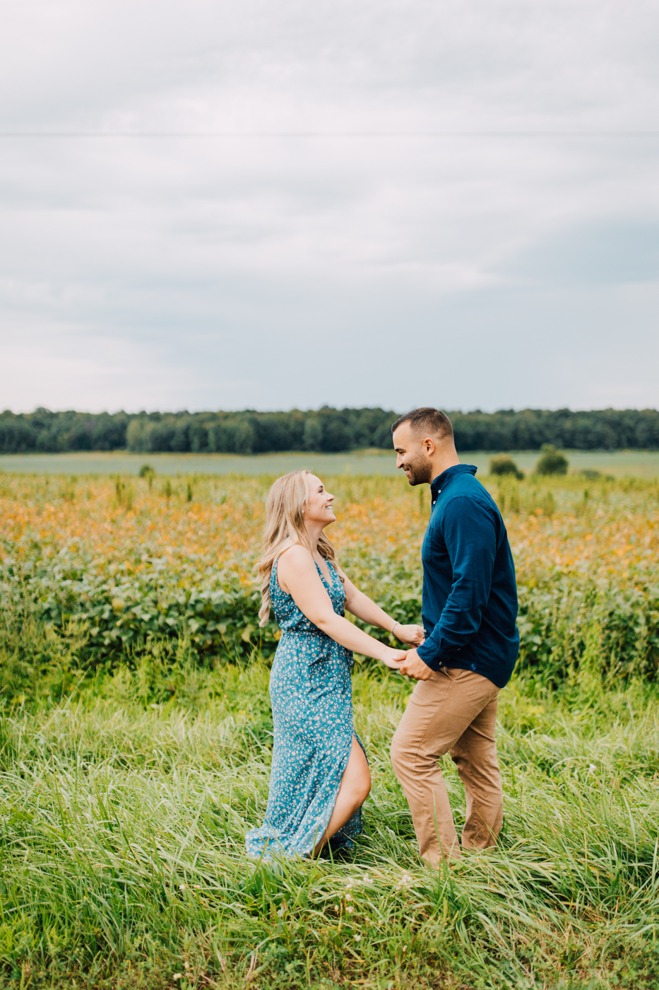  Engaged couple stands in a field of tall grass while taking classic engagement photos in Central NY 