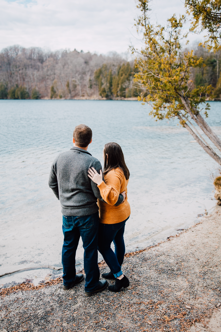  Engaged couple embraces as they look out over the lake during their engagement session at Green Lakes State Park 