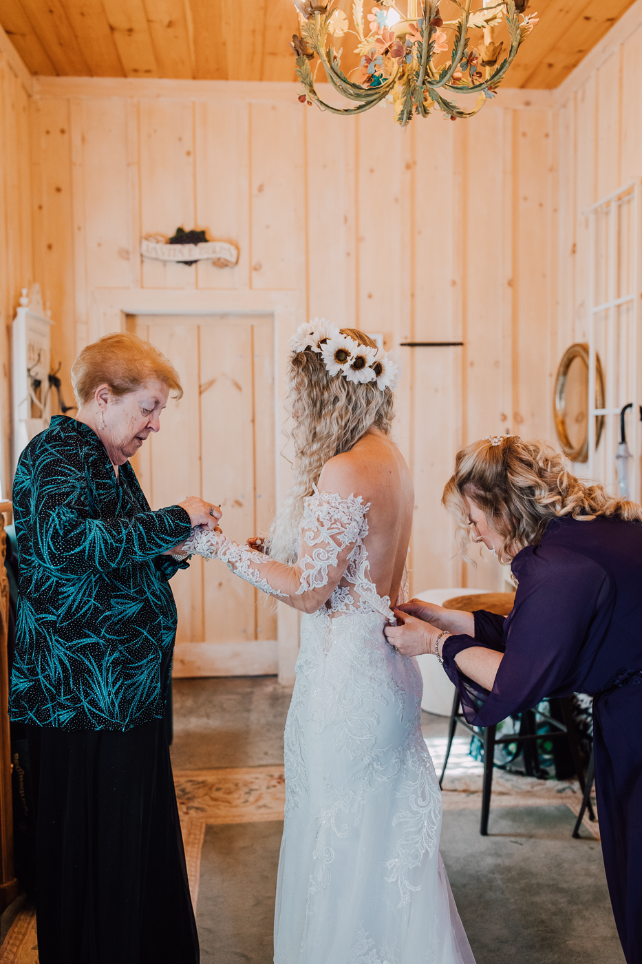  Bride is buttoned into her lace wedding dress while wearing a flower crown 