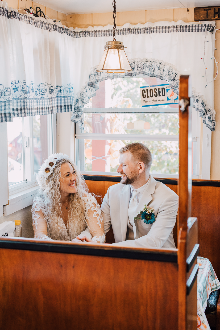  Bride and Groom sit side-by-side in a booth at a local diner as they take wedding photos in downtown Little Falls NY 