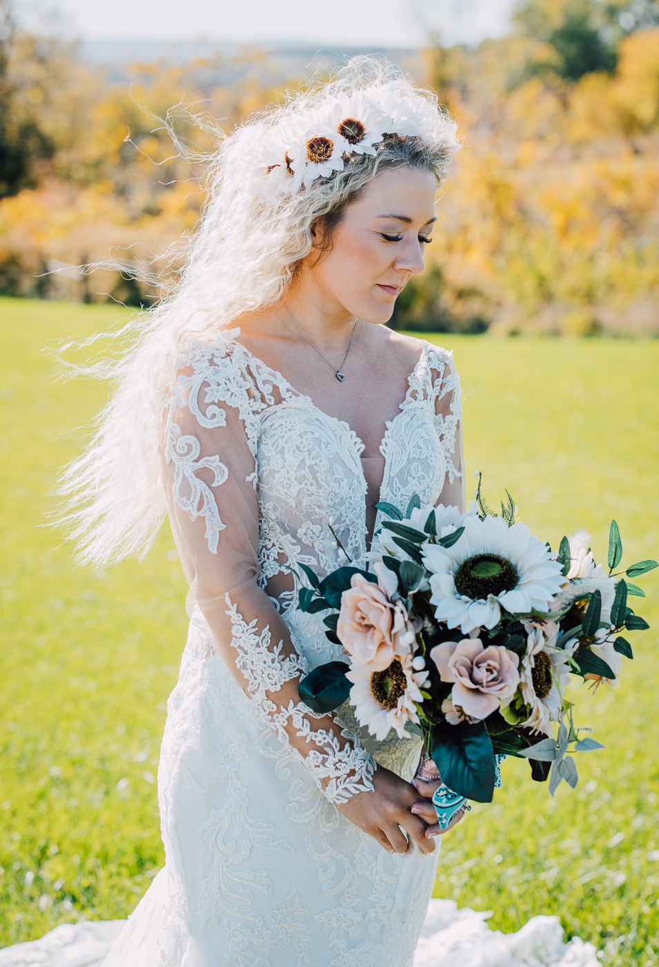  Bride poses for wedding photos, looking down at her bouquet with wild curly blonde hair, a flower crown, and a lace wedding dress 