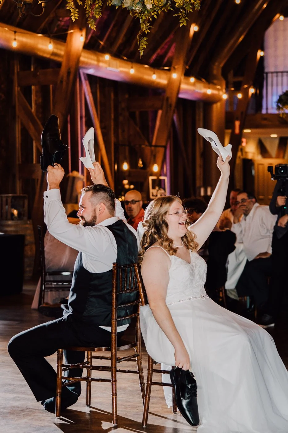  Bride and Groom hold up shoes during the Shoe Game at their barn wedding reception 
