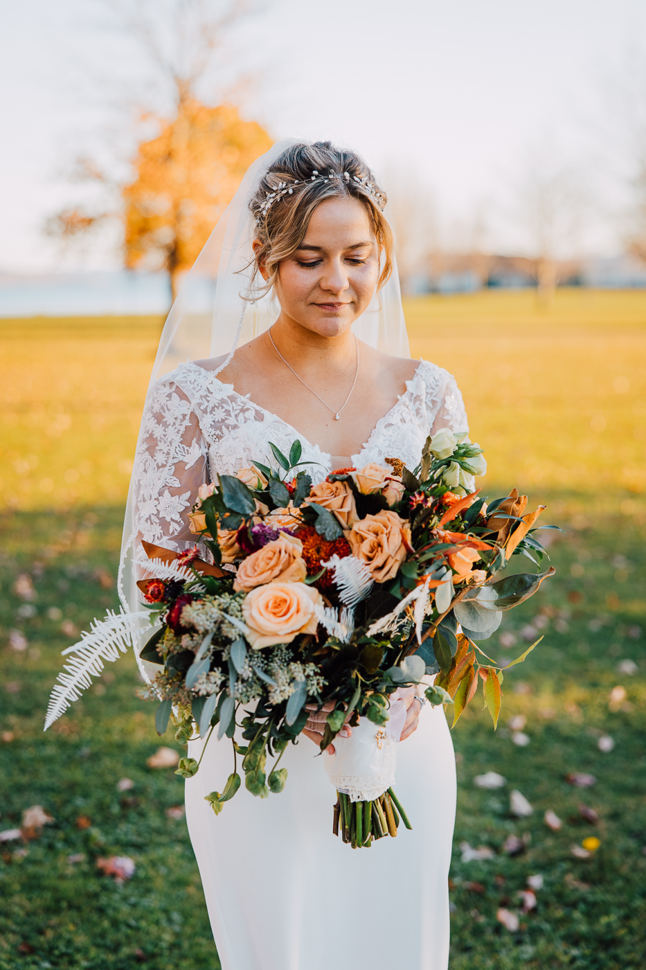 Bride takes wedding photos at Emerson Park Pavilion with lush fall wedding flowers, a simple veil, and long-sleeved lace wedding dress