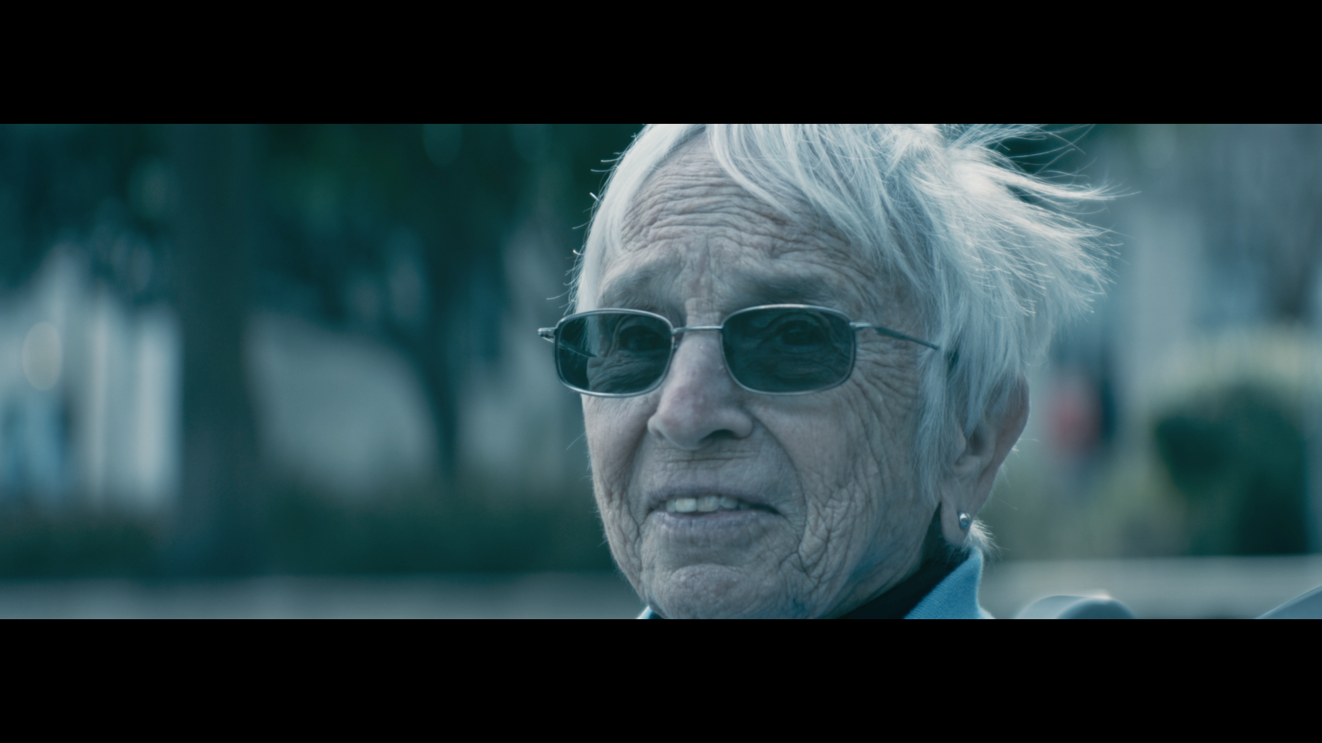 Close-up of an elderly woman with white hair, wearing sunglasses, outdoors on a sunny day.