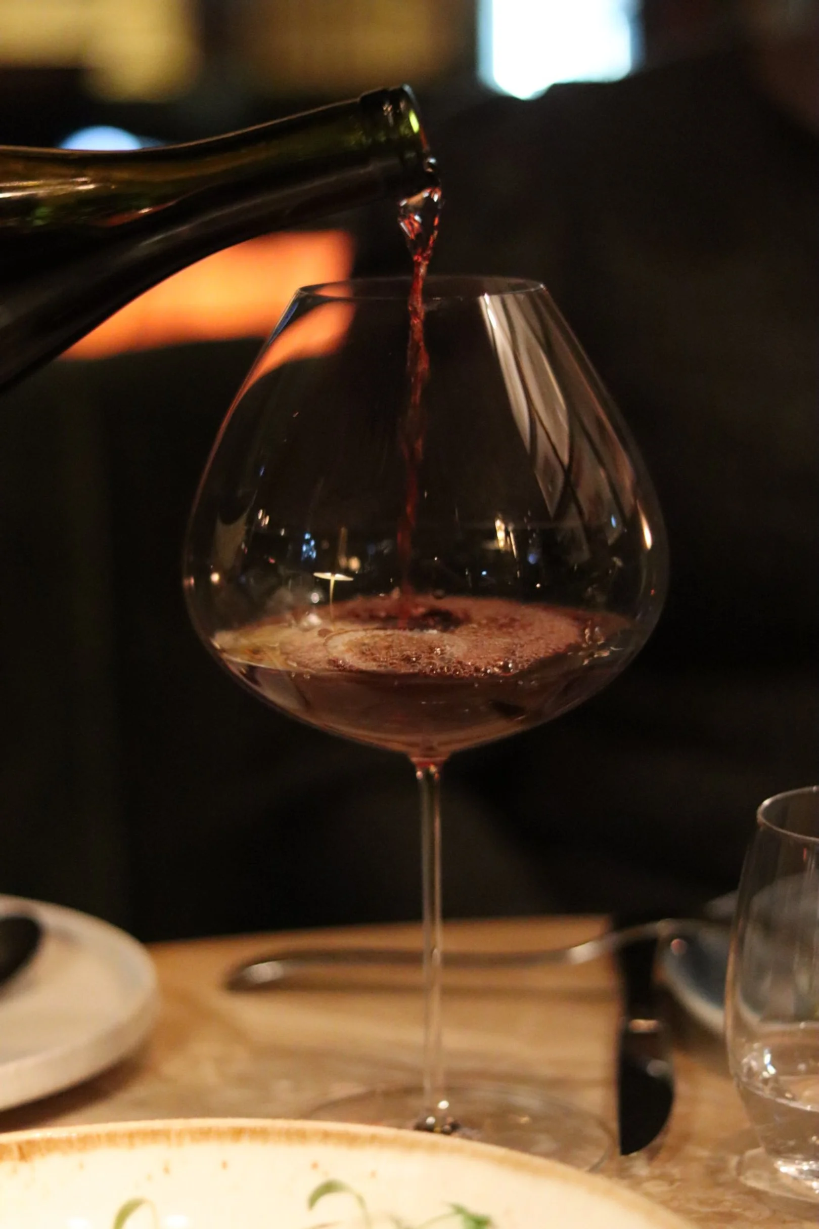 Rødvin som helles i vinglass ved bordet under middagsservering.