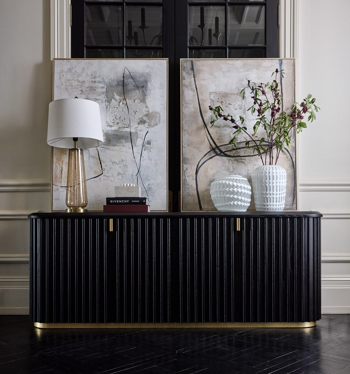A sleek black fluted credenza sideboard styled with modern vases and fine-art paintings, by Bakkes Images.