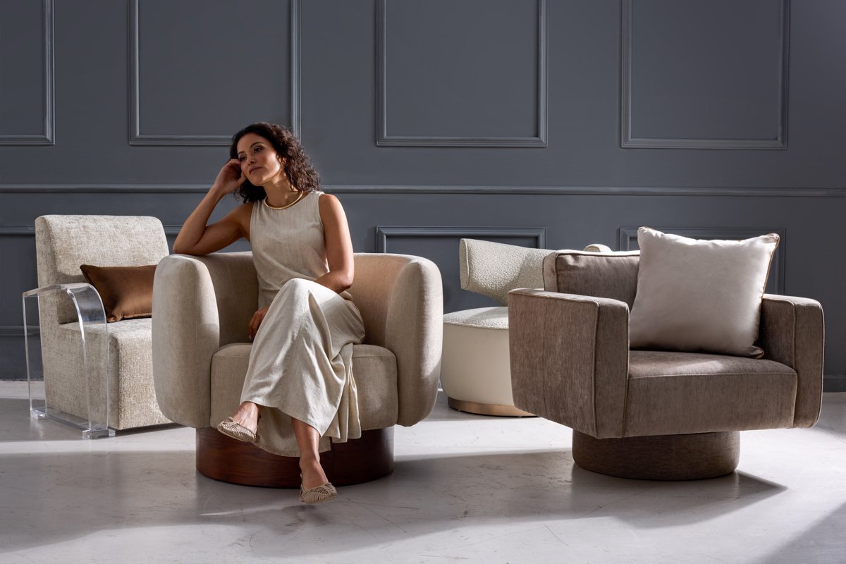 A woman sitting in a modern cream armchair inside a beautifully furnished studio living area, by Bakkes.