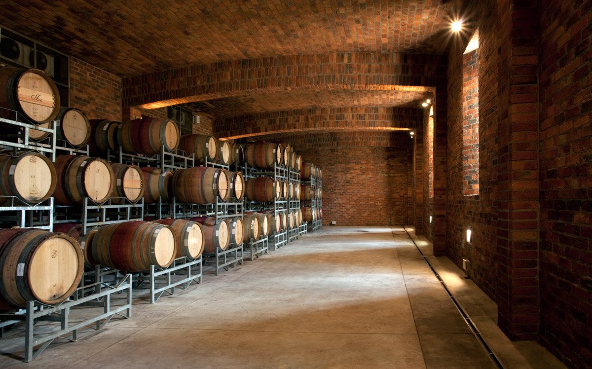 An impressive, long vaulted brick cellar hallway packed with premium oak aging barrels, by Bakkes Images.