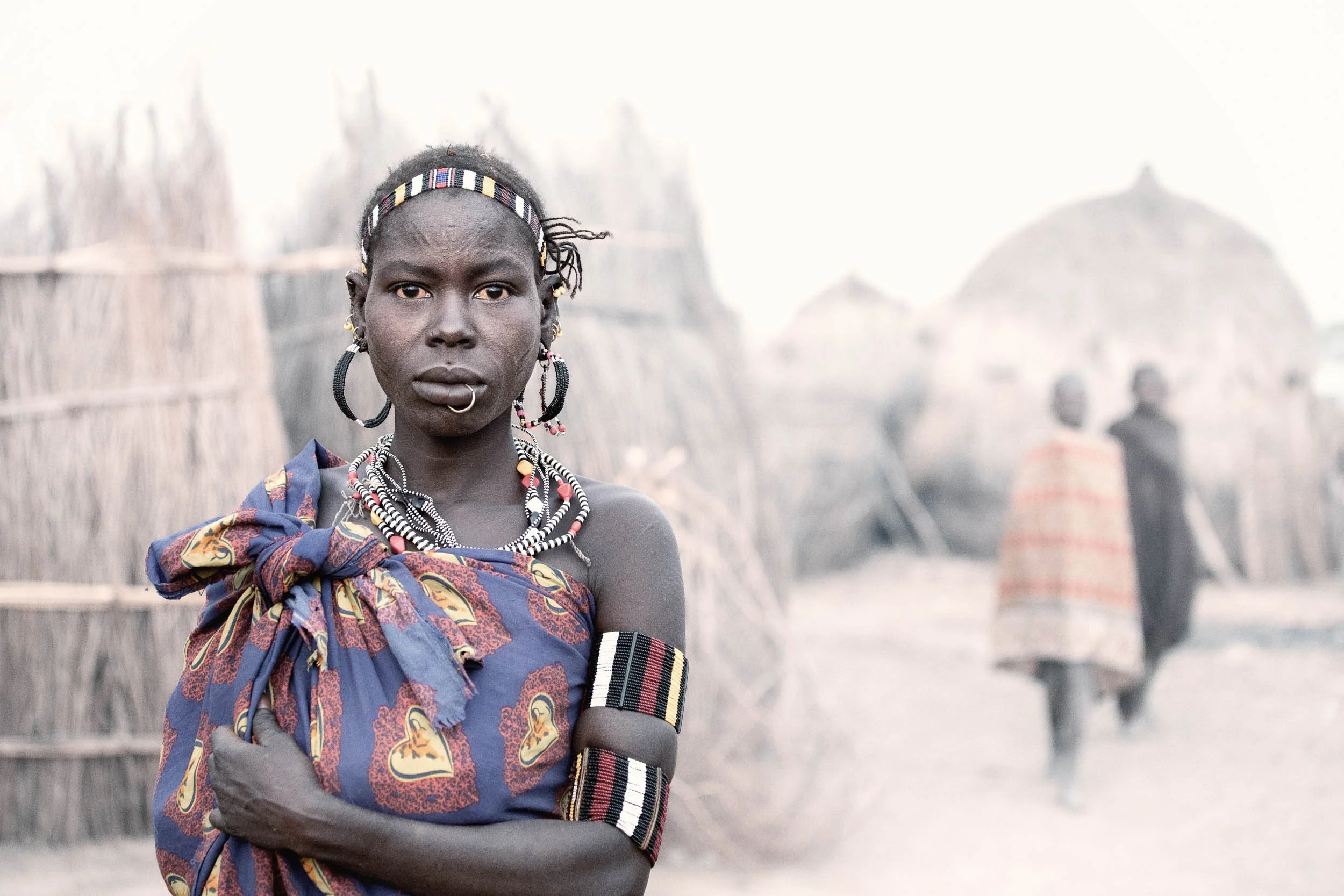 Jiye woman standing before traditional buildings, South Sudan